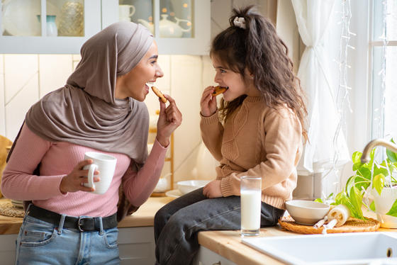 Muslim mother with hijab and her little daughter eating snacks in the kitchen.