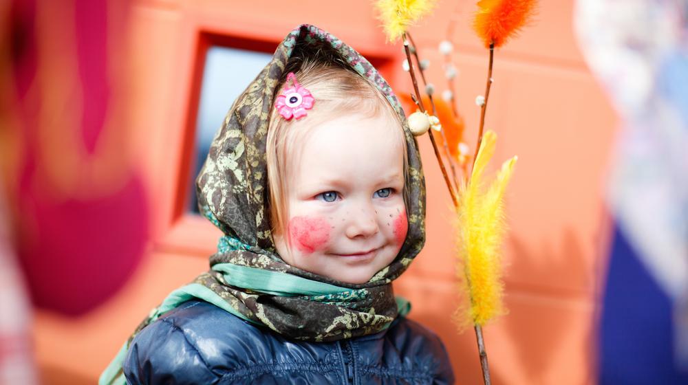 Kleines Mädchen mit roten Backen und Kopftuch trägt Palmkatzen zur Osterweihe.