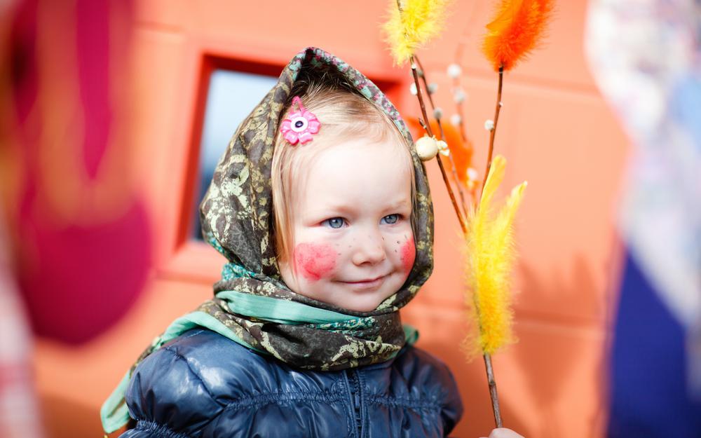 Kleines Mädchen mit roten Backen und Kopftuch trägt Palmkatzen zur Osterweihe.