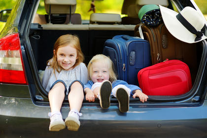 Zwei Schwestern sitzen im Kofferraum eines Autos beim Gepäck