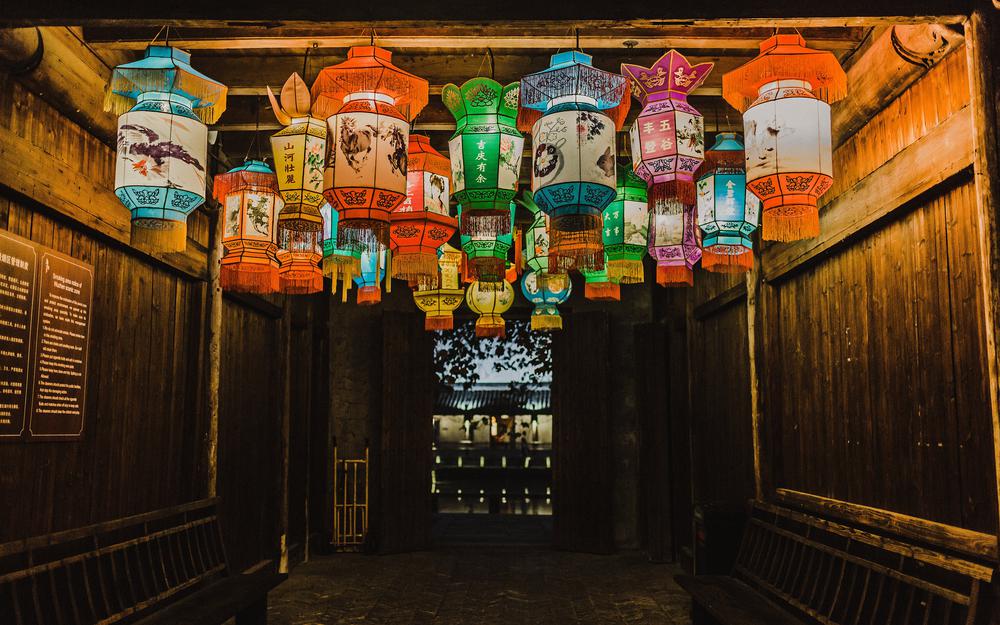 In einem asiatischen Zimmer mit Blick nach draußen auf eine Abendlandschaft befinden sich Dutzende bunte, hell erleuchtete Papierlampions.