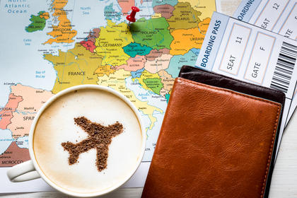 Landkarte, darauf Reisepässe und ein Cappuccino mit Kakaoflugzeug