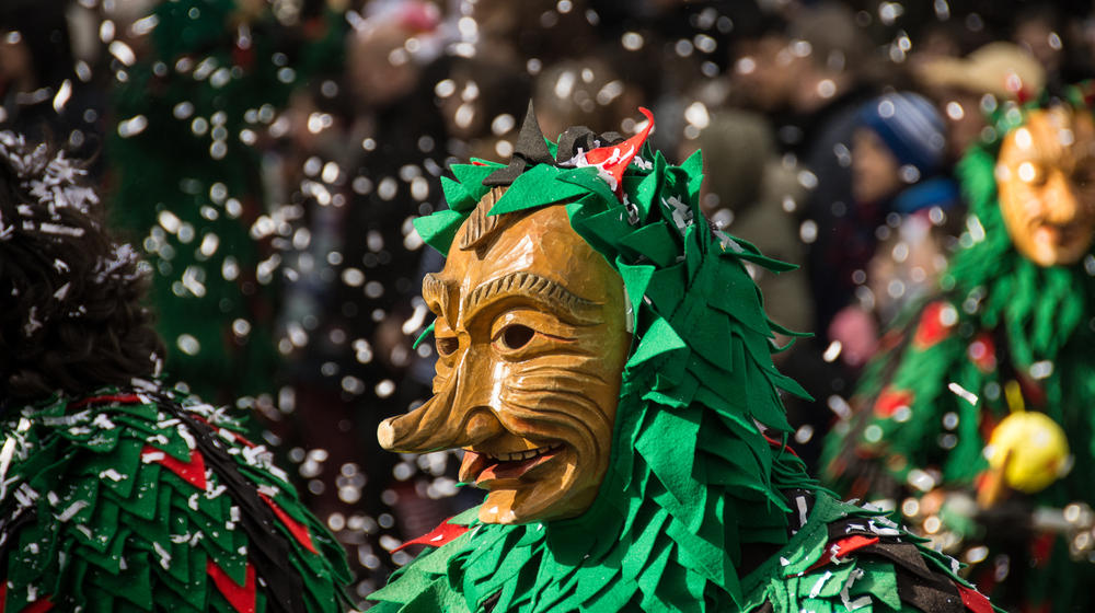Wooden carnival mask with green cape and confetti all around.