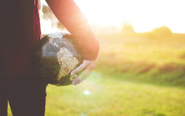 Sunlit meadow, a person holds a ball in the shape of the globe.