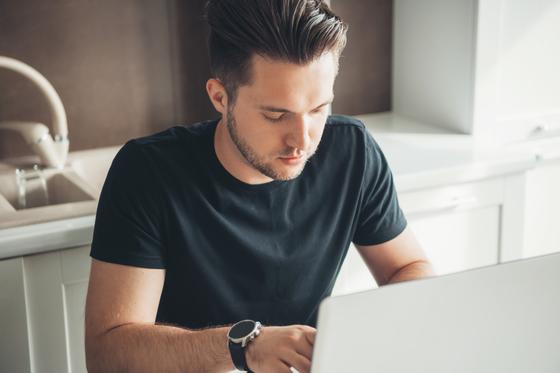 Junger Mann tippt konzentriert am Laptop 