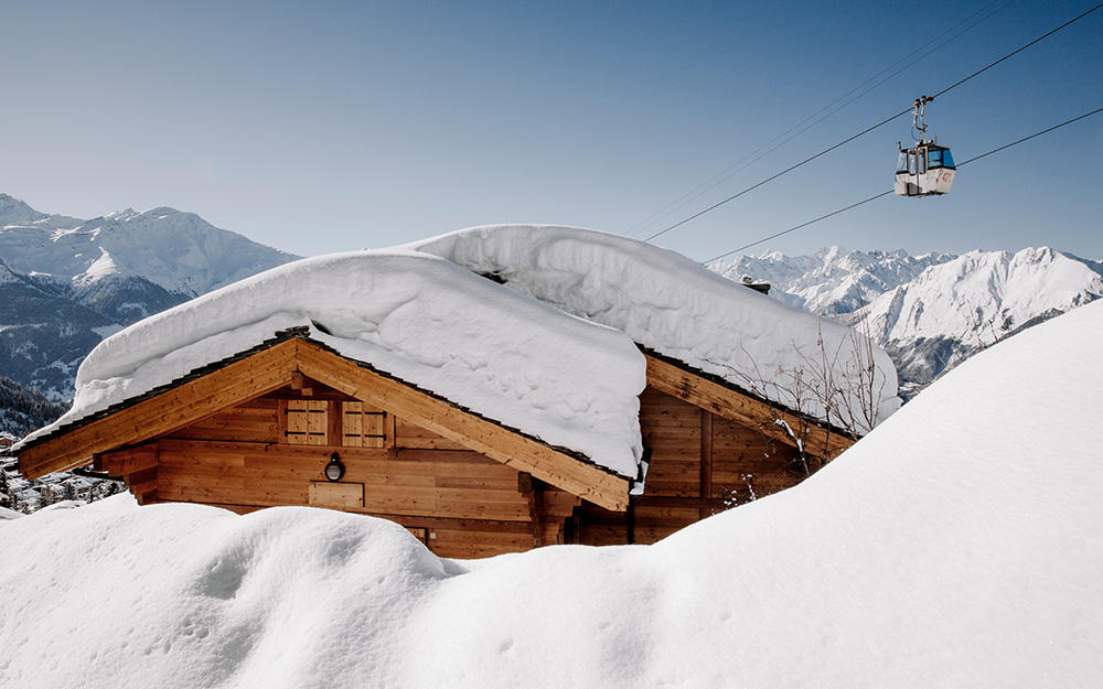 Eingeschneite Hütte in den Bergen neben einem Skigebiet