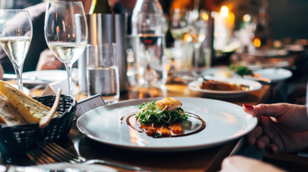 A table with half-filled water and wine glasses, a beautiful plate in front of it, and a dish artistically arranged in the middle.