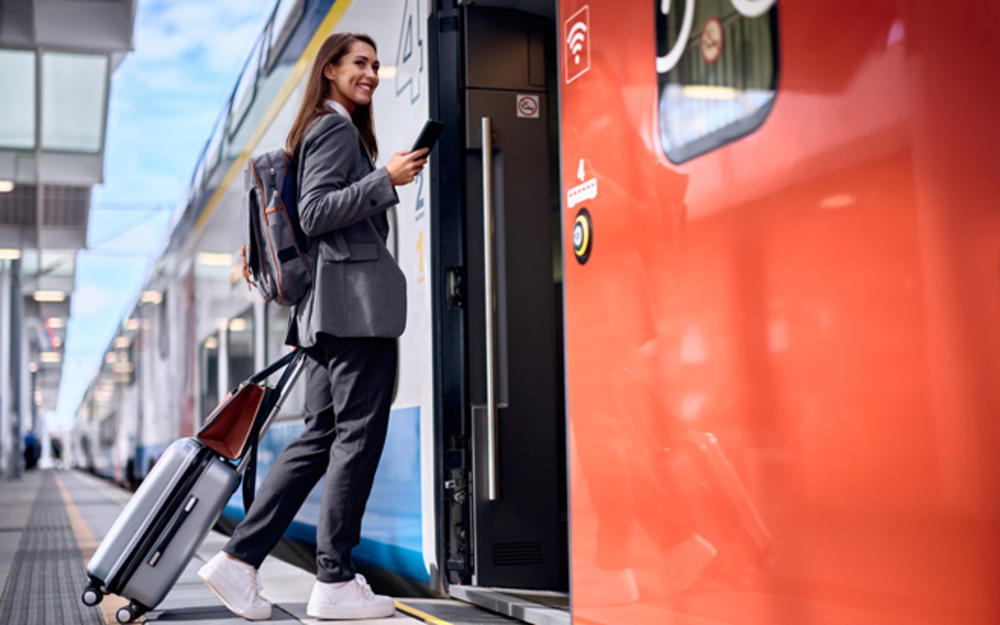 Eine Geschäftsreisende in den Mitzwanzigern in Anzug aber mit Turnschuhen steigt lächelnd in den Zug ein.
