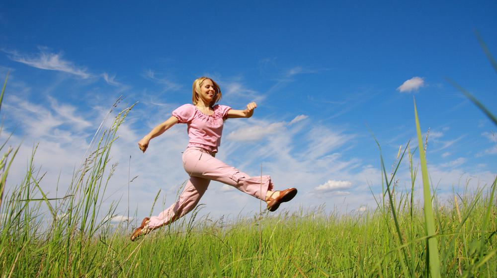 Young woman enjoys jumping and running across a meadow.