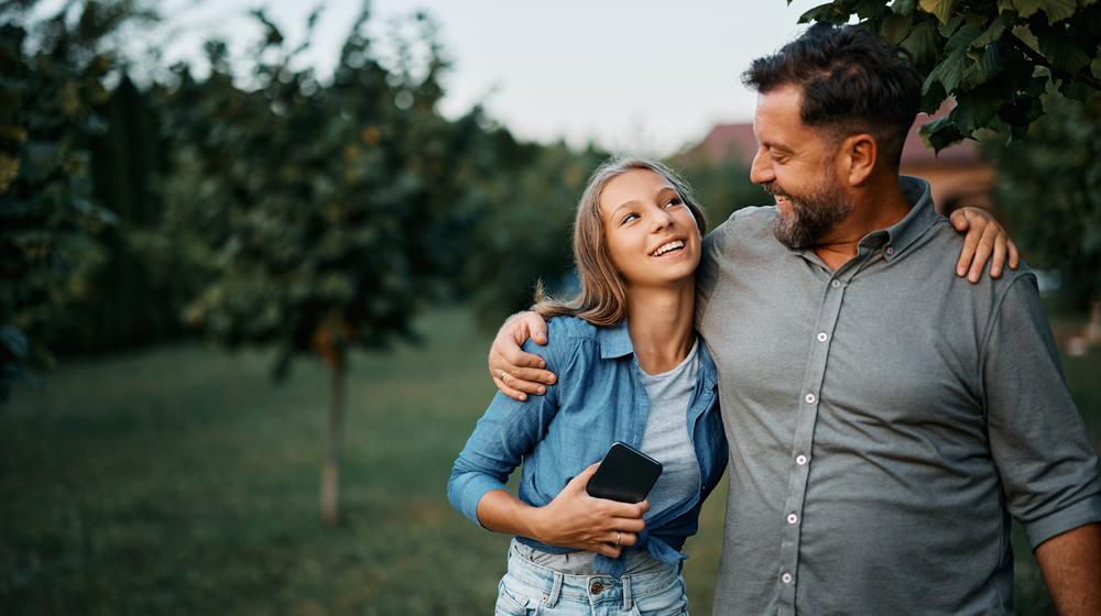 Proudly smiling man hugs his teenage daughter on the shoulder.