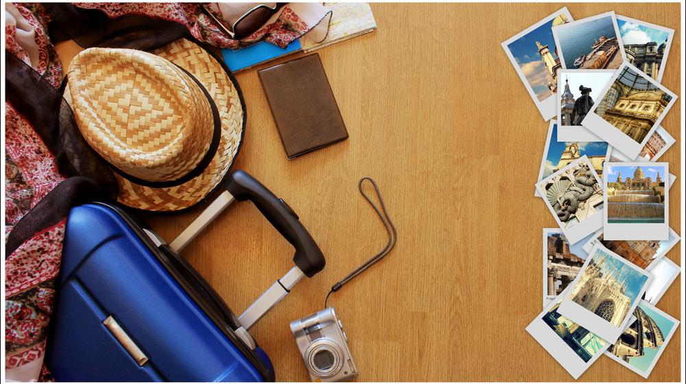 Am Boden liegen diverse Fotos von Reisezielen, ein Strohhut, daneben ein Koffer.