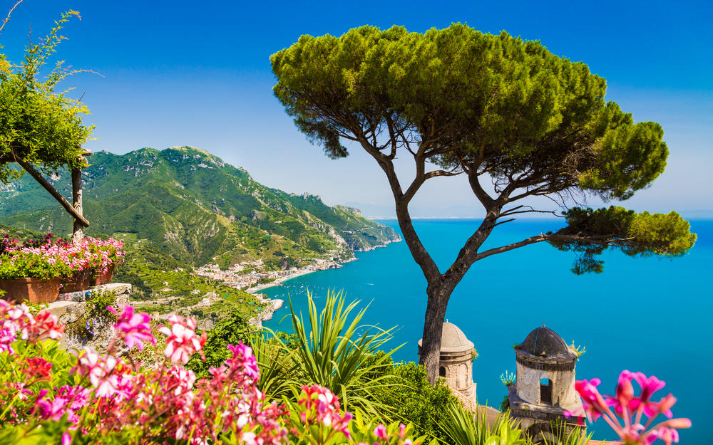 Italien, Kampanien, die Amalfiküste mit Blüten und Baum im Vordergrund, dahinter das Meer und die Küste.