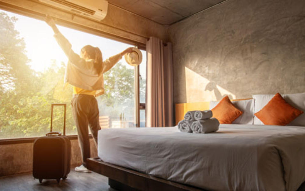 Junge Frau genießt die Abendsonne bei der Ankunft in ihrem Hotelzimmer und streckt dabei die Arme aus.