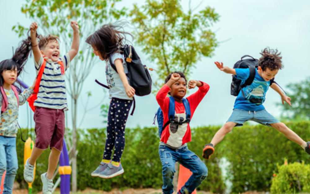 Fünf Erstklassler mit Schultasche am Rücken springen vor Freude in die Luft.