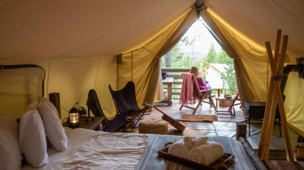 Von einem luxuriösem Campingzelt sieht man nach außen, davor sitzt eine Frau ganz gemütlich.