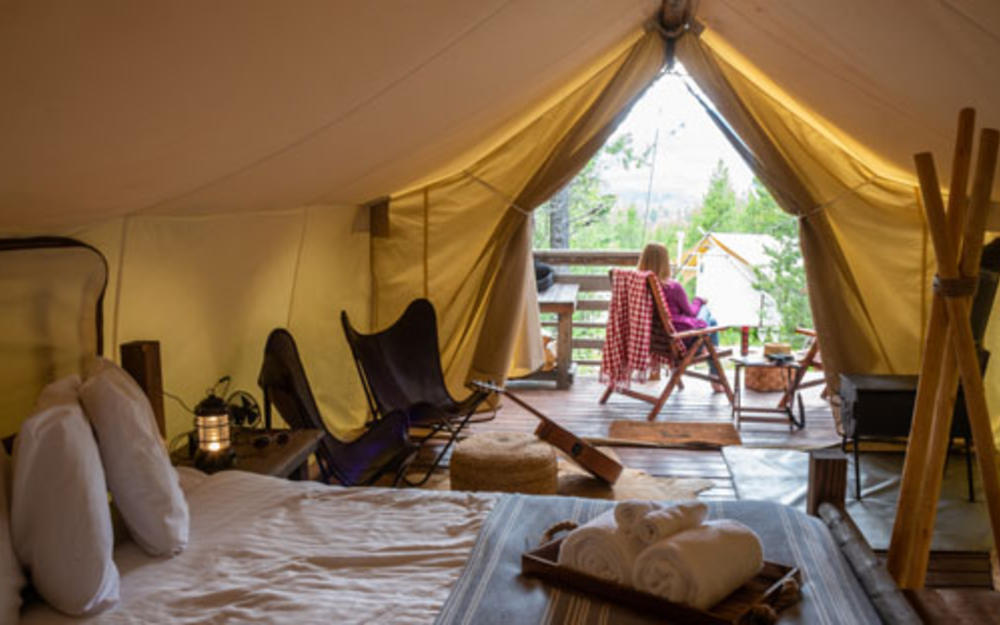 Von einem luxuriösem Campingzelt sieht man nach außen, davor sitzt eine Frau ganz gemütlich.