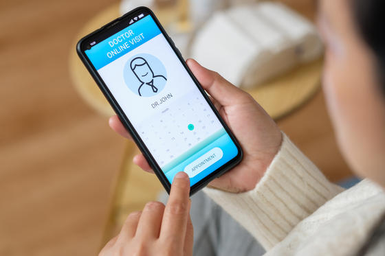 A woman is holding a mobile phone in her hand, displaying the contact details of a doctor.