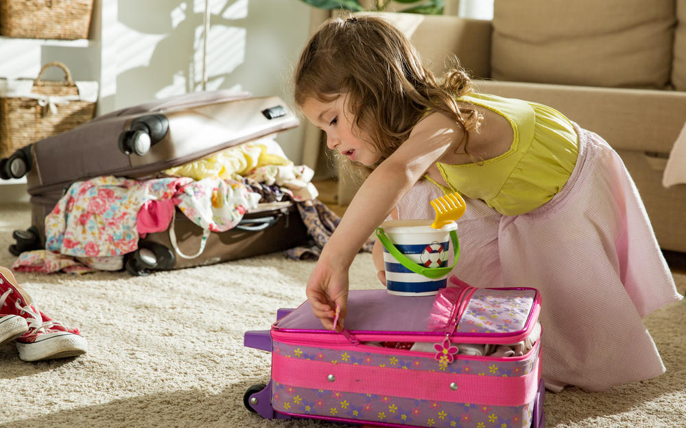 Kleines Mädchen sitzt am Teppich und schließt den eigenen, rosa, Koffer.