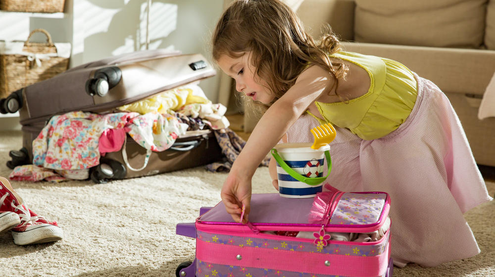 Kleines Mädchen sitzt am Teppich und schließt den eigenen, rosa, Koffer.