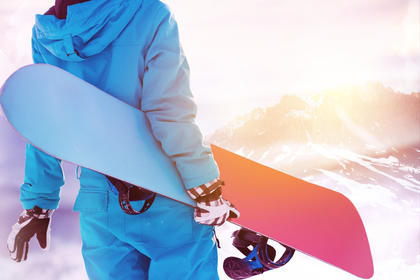 Frau mit blauem Schianzug und Snowboard am Berg