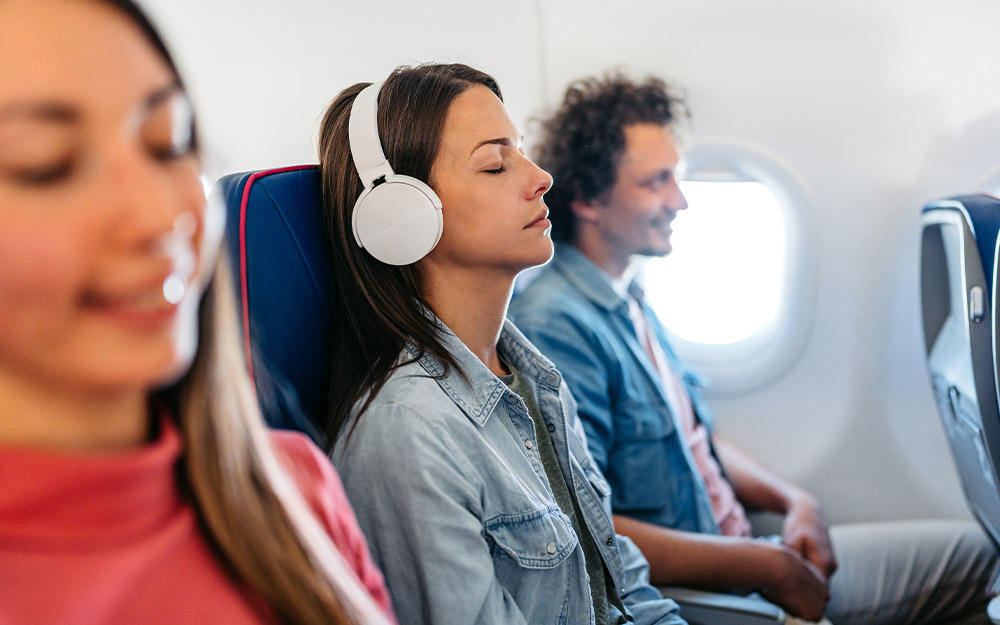 Junge Frau mit Kopfhörern schläft ruhig im Flugzeug