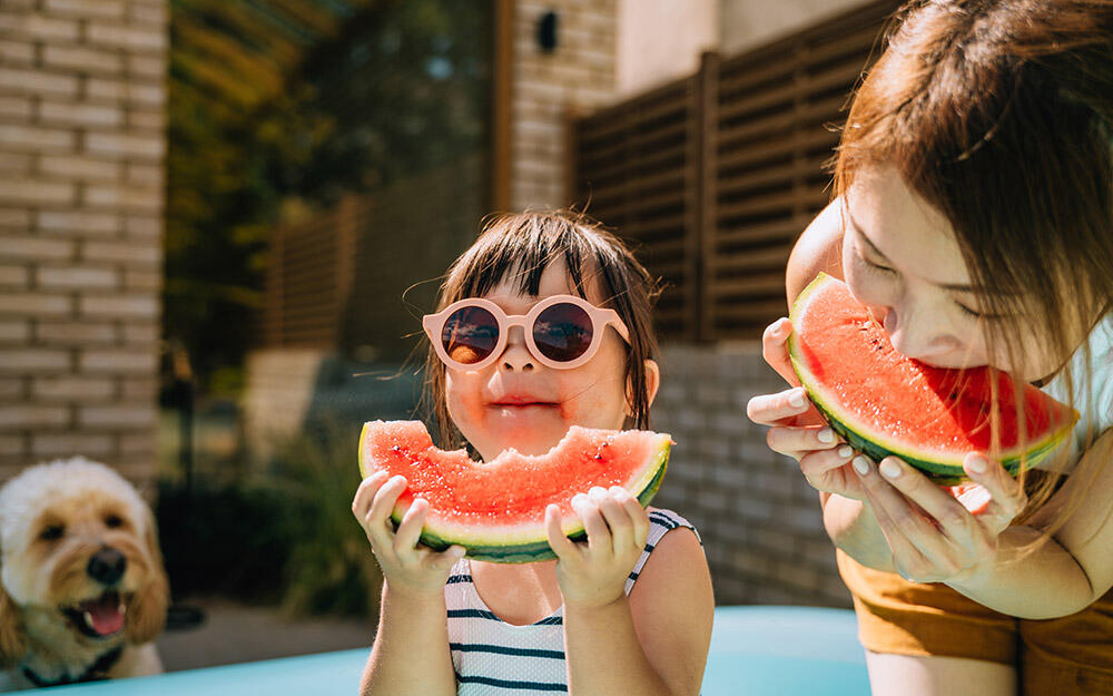 Mother and child wearing sunglasses enjoy a refreshing slice of watermelon