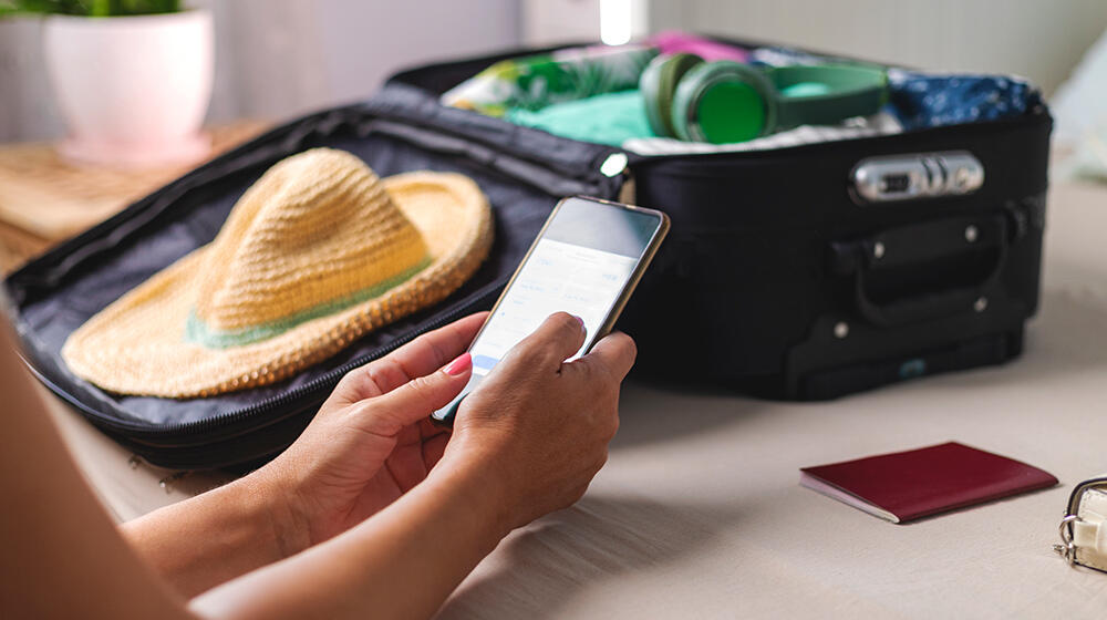 Nahaufnahme einer Frau bei der Reisevorbereitung: Sie hakt wichtige Notizen auf einer Checkliste auf ihrem Smartphone ab