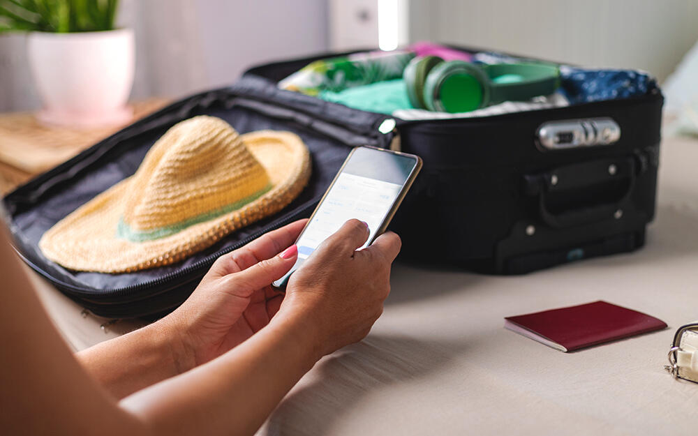 Close-up of a woman preparing for a trip: she ticks off important notes on a checklist on her smartphone.