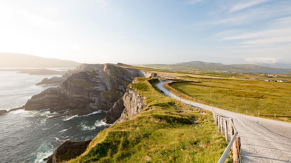 Straße durch grüne Landschaft entlang einer felsigen Steilküste Irlands