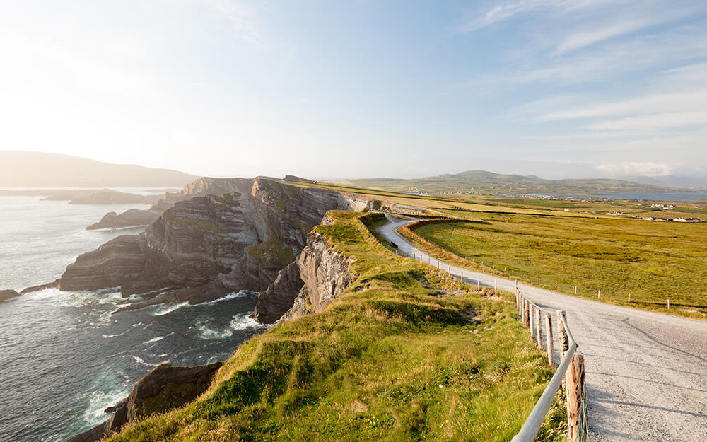 Road through green countryside along a rocky Irish cliff coast