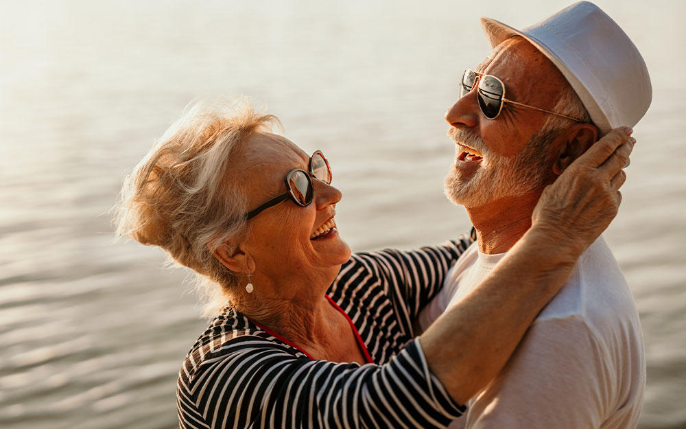 Frau und Mann mit Sonnenbrillen tanzen glücklich lachend am Strand