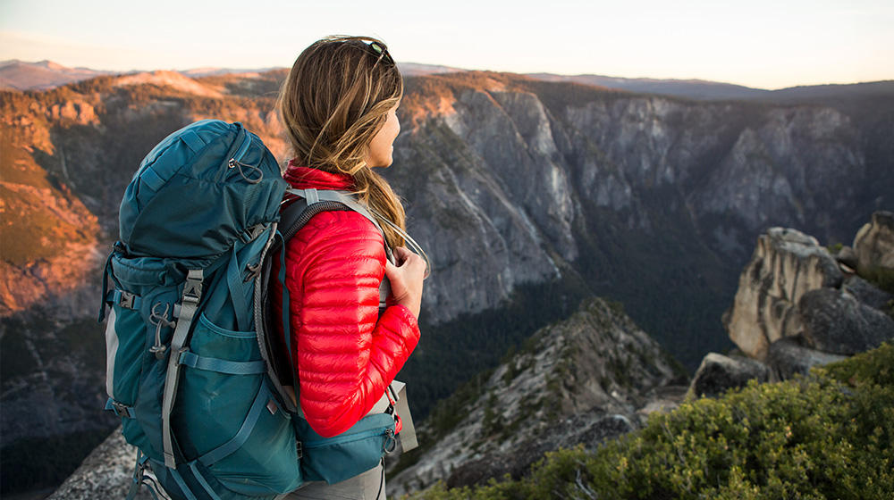 Young woman with a backpack enjoying the wide view of an untouched rocky landscape at sunset