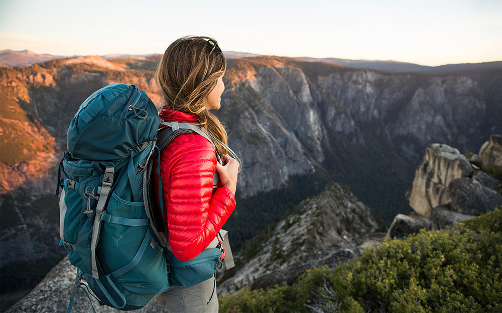 Young woman with a backpack enjoying the wide view of an untouched rocky landscape at sunset
