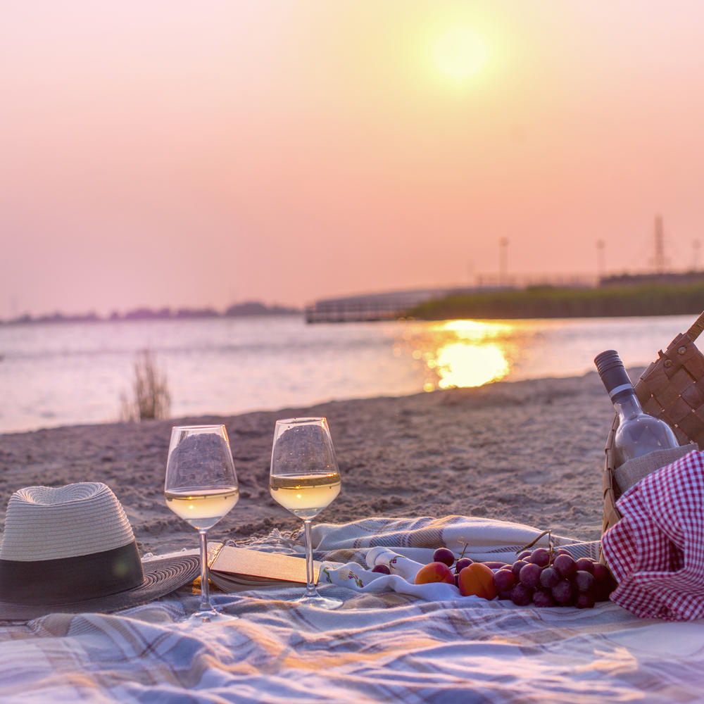Picknickdecke mit Weingläsern vor Sonnenuntergang am Strand