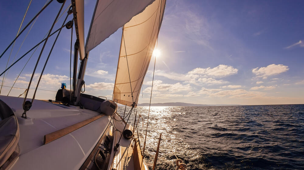 Sailing ship on the calm open sea heading toward the sunset